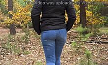 Eine Teenager-Freundin in einer blauen Jeanshose zeigt aufreizend ihren knackigen Po in einem Waldstück